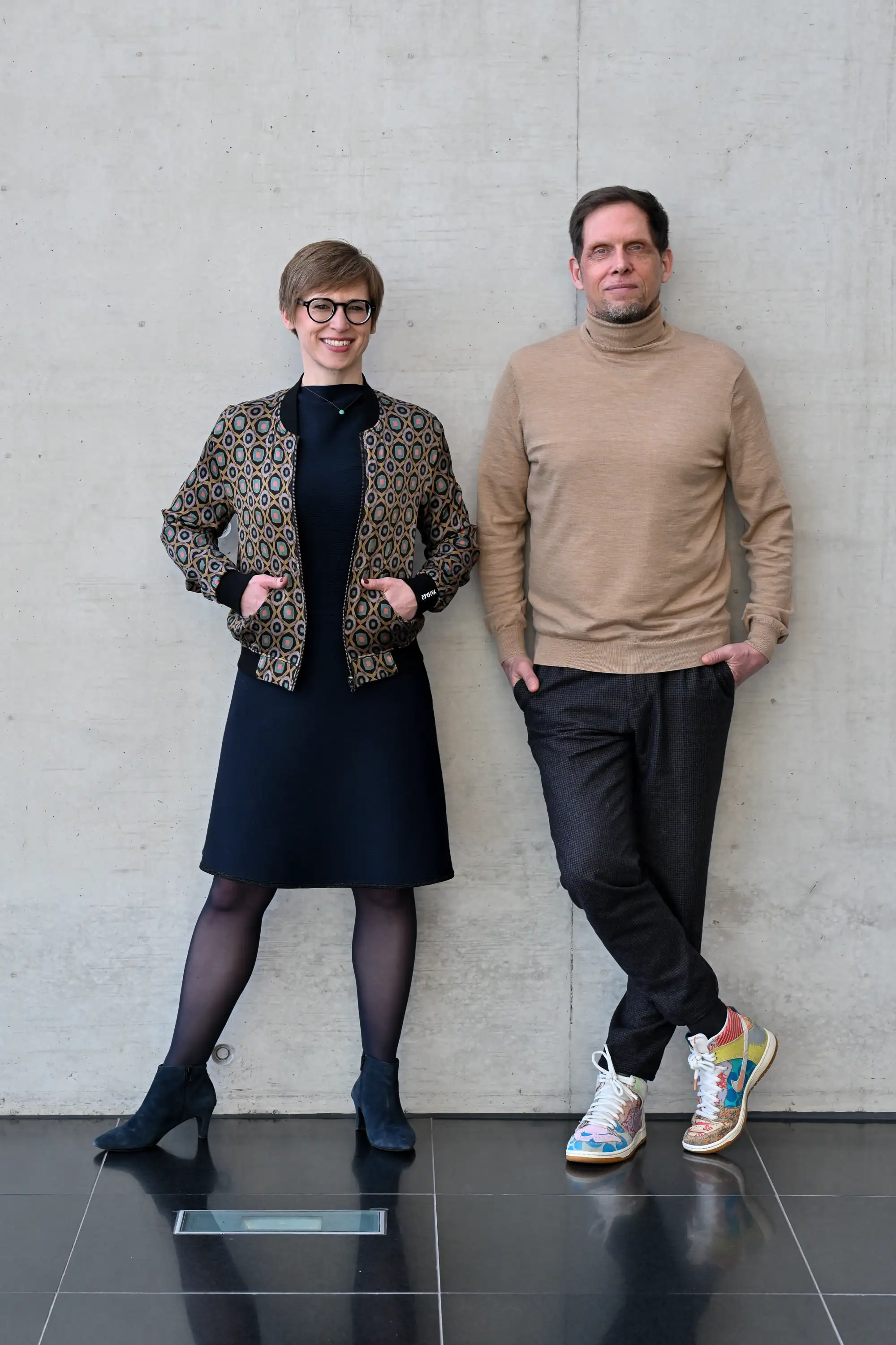 Swantje and Peter standing in front of a wall and looking at the camera