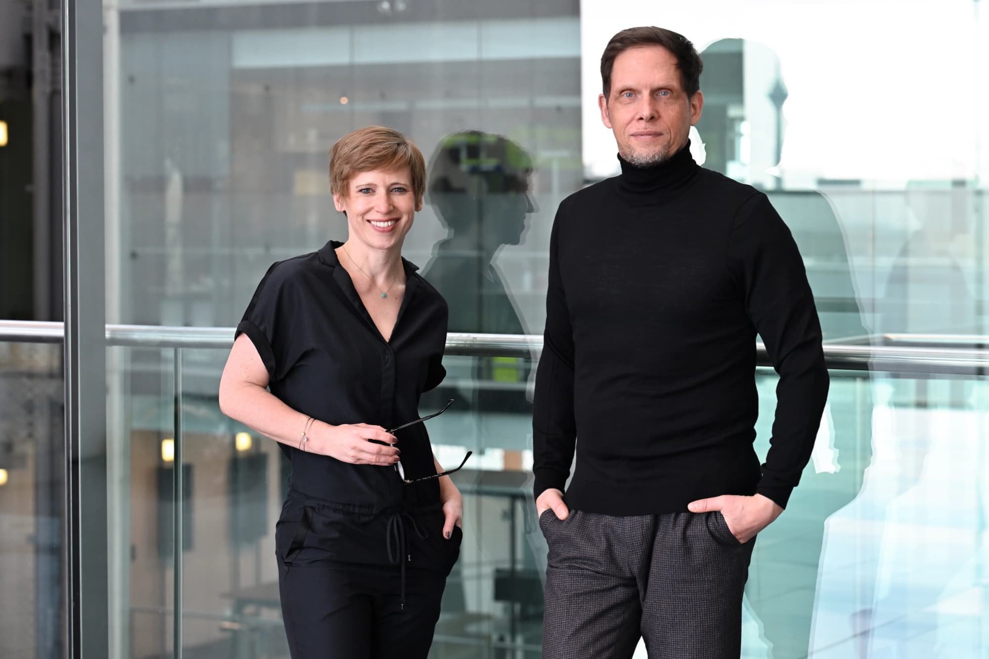 Swantje and Peter standing in front of a glass wall and looking at the camera